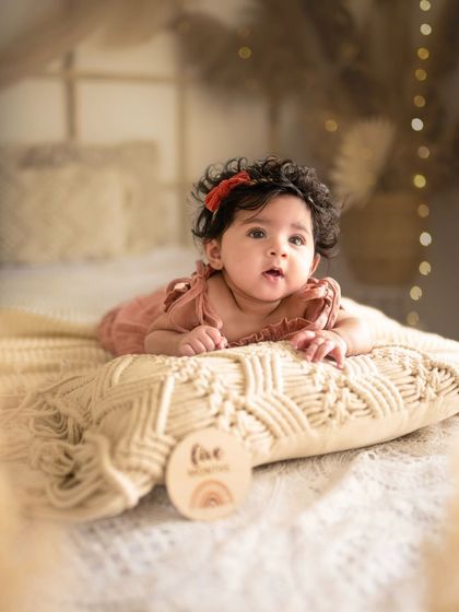 Five months old and full of wonder. This baby is lying on a macrame pillow, part of a beautiful bohemian-inspired setup for her milestone session.