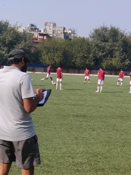 A coach observes a match with a clipboard in hand, analyzing player positioning and team shape. Constant evaluation is key to tactical improvement.