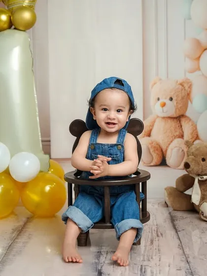 A full-length portrait showing the complete first birthday setup, with the "ONE" balloon, teddies, and a very happy baby boy in his cute denim outfit.