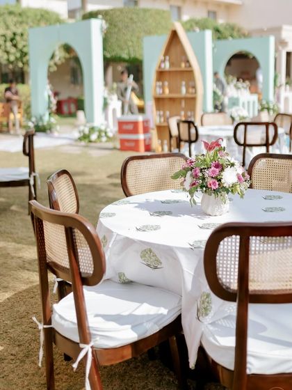 Guest seating at the pastel Mehendi, with elegant wooden chairs and tables dressed in custom block-printed linens, all contributing to a chic, garden-party feel.