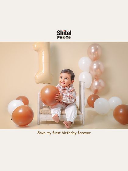 A happy one-year-old playing with balloons. The simple, neutral-toned setup keeps the focus on the baby's joyful expression.