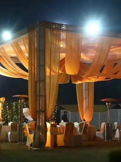 An outdoor seating area for a night event. The space is lit by large heaters and features a canopy with warm orange drapes, creating a cozy atmosphere.