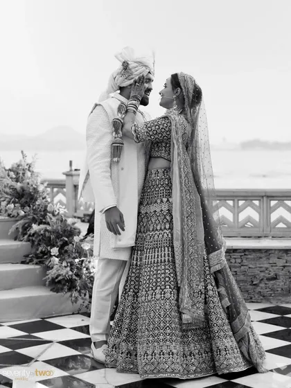 A classic black and white portrait of the couple on their wedding day in Udaipur, with the serene lake and City Palace in the background.