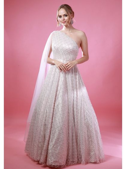 A full-length shot of Irina Rudakova in a sparkling white one-shoulder gown, showcasing the entire elegant ensemble against a solid pink studio background.