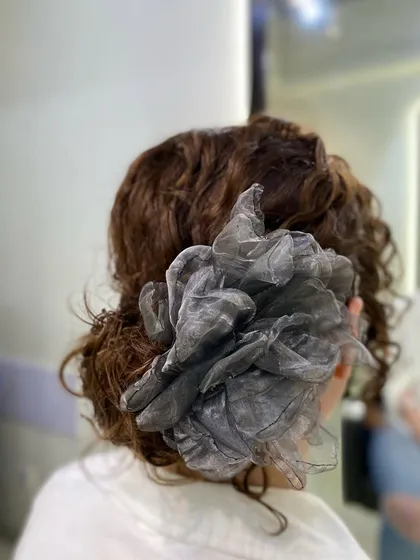 This is an example of an elegant curly updo, a beautiful protective style perfect for a special event. I created this soft, romantic look by carefully pinning the curls to create volume while keeping them secure, finishing it with a delicate fabric flower accessory.