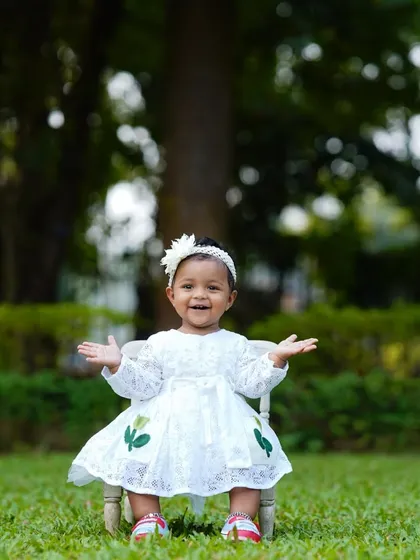 With her arms wide open, this little girl in a white dress is ready for a hug. A simple, joyful moment captured in a natural park setting.