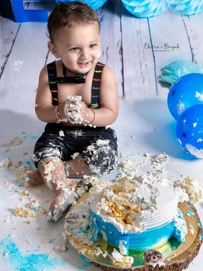 Another angle of the messy fun, showing the little boy with cake on his hands, feet, and face during his first birthday photoshoot.