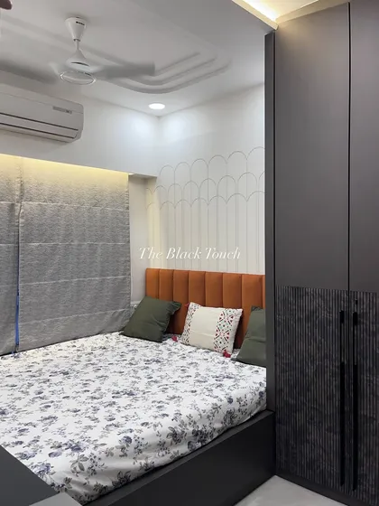 This bedroom features a dark, textured wardrobe and an orange upholstered headboard, creating a bold contrast. The scalloped wall paneling behind the bed adds a subtle, decorative touch to the room.