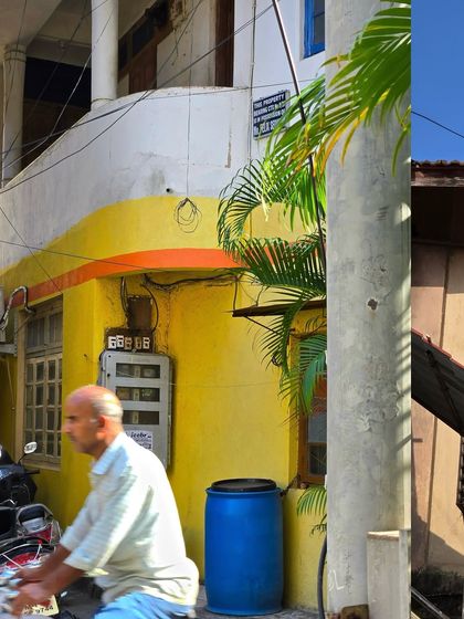 A man on a scooter rides past a yellow-painted house in Bandra.