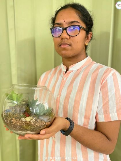 A proud creator holding her finished round bowl terrarium, a beautiful, self-contained ecosystem she built herself.