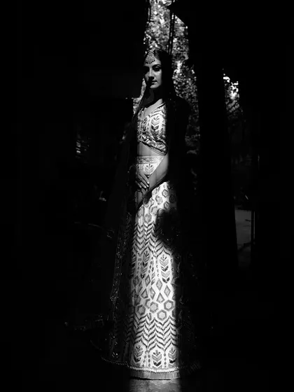 An artistic black and white shot where the model is almost entirely in shadow, with only the white embroidered lehenga illuminated. This play of light and dark creates a mysterious and dramatic effect.
