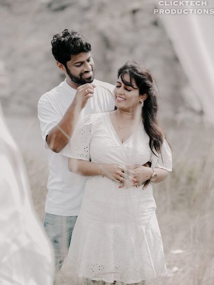 A sweet interaction between a couple in a field, with the groom playfully touching the bride's hair.