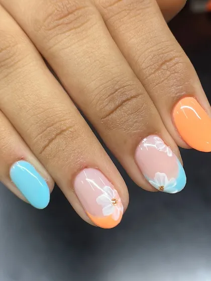 A relaxing holiday vibe on your nails. This design combines a classic French with a twist, using pastel orange and blue tips and a delicate white flower accent.