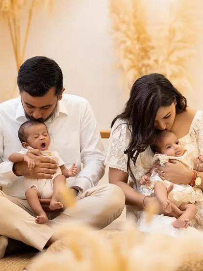 Capturing the real, unposed moments of newborn life. Here, one twin lets out a big yawn while the other is kissed by their mother, showing the sweet, authentic side of a twin family photoshoot.