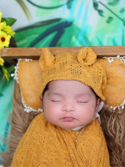 A close-up of a baby in a jungle-themed shoot, wearing an adorable elephant-ear bonnet. The yellow tones and sunflower accents create a warm and cheerful atmosphere.