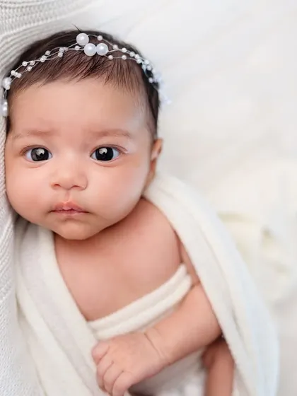 A close-up portrait of a beautiful newborn with a pearl headband. We use minimal, elegant props to enhance your baby's natural beauty.