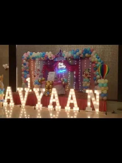 A candy-themed stage setup with large light-up letters. The backdrop includes a neon sign and fairy lights, creating a bright and exciting atmosphere for a first birthday.