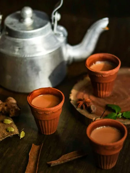 A rustic chai setting featuring traditional kulhads (clay cups) and a classic kettle. The styling with whole spices like ginger and cardamom adds an authentic touch.
