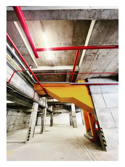 The basement car park of "The Treehouse" is treated with the same design rigor as the rest of the building. Exposed services are organized and painted, with a yellow staircase adding a surprising element of color.