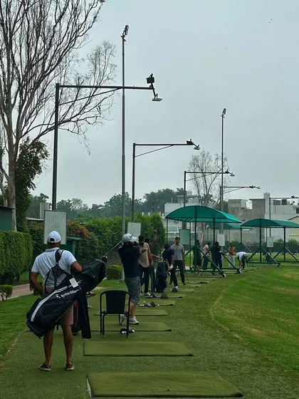 A golfer with his bag on his shoulder walks along the range, ready to find his spot and start the grind.