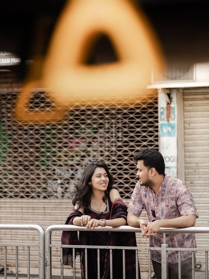 A creatively framed shot of a couple leaning against a railing, their conversation captured through a foreground element.