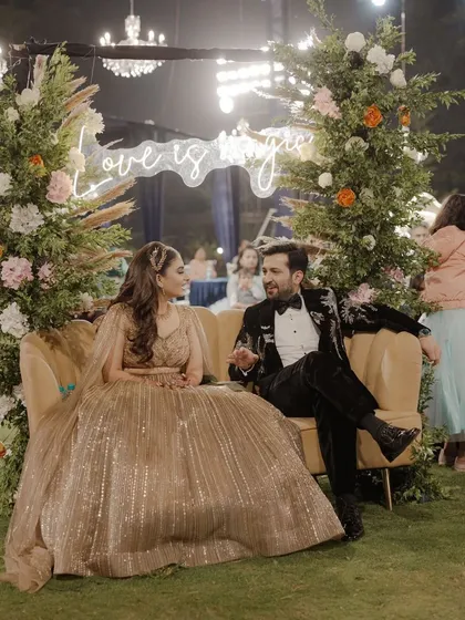 A romantic couple seating area for a Sangeet, with a 'Love is Magic' neon sign and a beautiful floral arch. It's the perfect cozy spot for the couple to enjoy the evening.