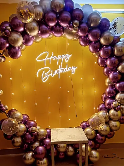 A gorgeous balloon ring in shades of purple and silver chrome. The backdrop is lit with fairy lights, and a neon 'Happy Birthday' sign adds the final touch.