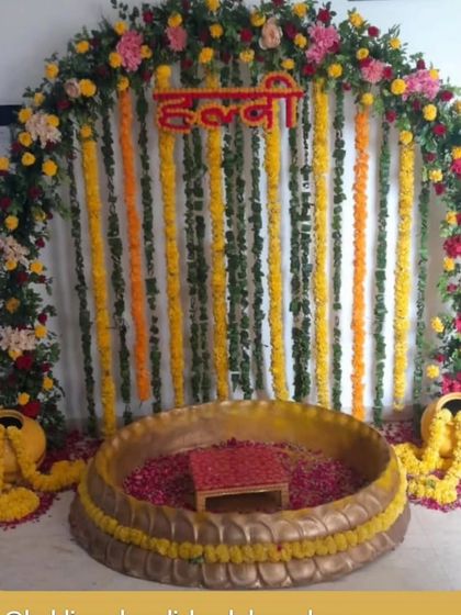 A beautiful Haldi setup with a floral arch and strings of marigolds. The large brass urli is filled with flower petals, ready for the ceremony, creating a classic and auspicious look.