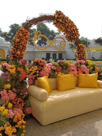 A vibrant Haldi seating area bursting with colorful flowers. The mix of orange, yellow, and pink creates a joyful and energetic atmosphere.