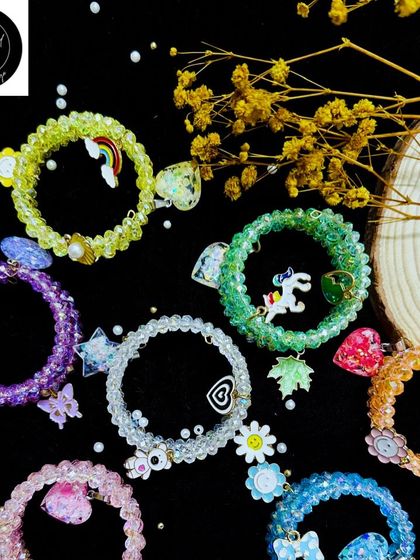 A collection of sparkly beaded bracelet rakhis for kids. These feature fun charms like unicorns, rainbows, and flowers, making them a delightful treat.