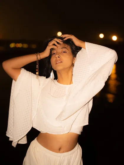 A powerful, direct-to-camera portrait. The simple white top and the dark, empty background make for a very striking image.