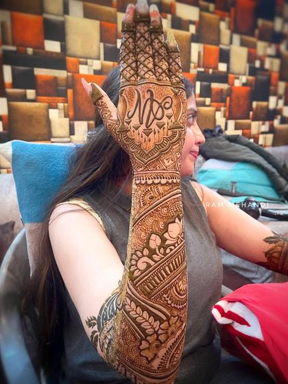 A beautiful full arm design featuring a large initial monogram on the hand, surrounded by intricate floral and traditional Indian patterns.