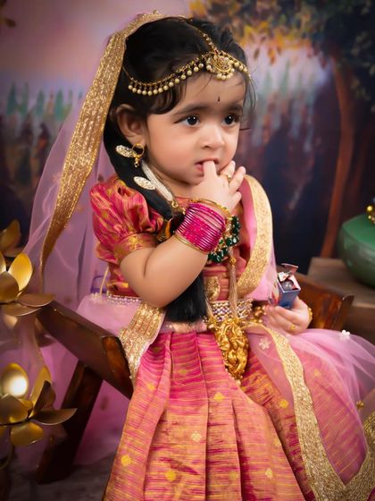 A beautiful little girl dressed as Radha, looking thoughtful and sweet. The rich pink and gold of her traditional dress are absolutely stunning.