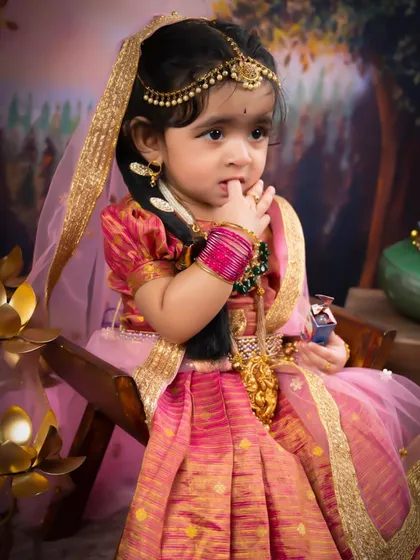 A beautiful little girl dressed as Radha, looking thoughtful and sweet. The rich pink and gold of her traditional dress are absolutely stunning.