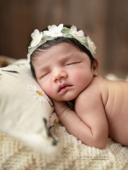 A close-up of a one-week-old baby girl, sleeping peacefully on a daisy-print pillow. The simple, natural elements make this a timeless and sweet portrait.