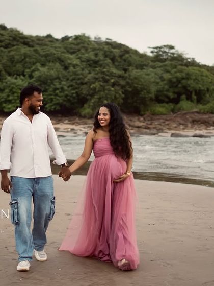 Walking hand in hand along the beach, with the lush greenery and ocean as their backdrop. This wide shot captures the beautiful scenery of an outdoor maternity session.
