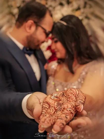 A creative close-up of the engagement ring resting on the bride's henna-adorned hand, with the couple blurred in the background.