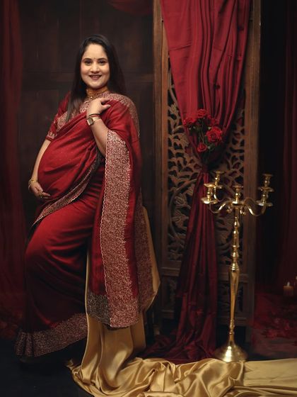 A solo portrait showcasing the beauty of a red embroidered saree. The mom-to-be looks powerful and elegant against the rich, warm tones of the studio set.