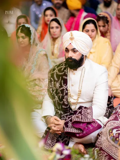 A candid shot of the groom during the Anand Karaj, listening intently to the Gurbani. The focus is on his respectful and serene demeanor.