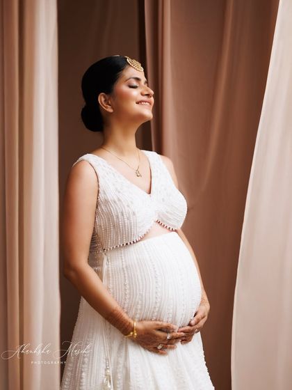 A moment of pure bliss, with eyes closed and a gentle smile, wearing a modern white two-piece outfit that celebrates the bump.