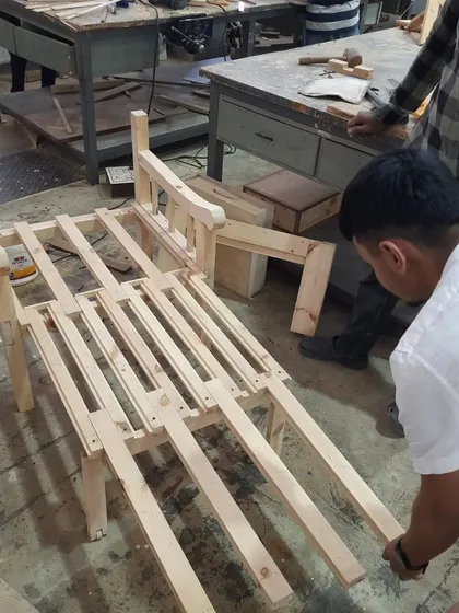 A student carefully fits the final slats into the frame of a lounge chair during the assembly phase.