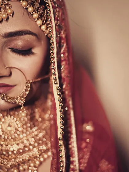 A stunning, artistic close-up of a bride in a red veil. The focus on her traditional nath (nose ring) and serene expression creates a powerful and timeless bridal portrait.