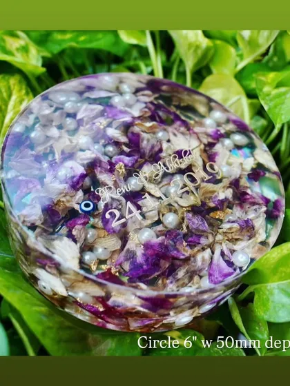 This 6-inch circular keepsake beautifully preserves purple and white varmala flowers, mixed with delicate pearls. The evil eye charm adds a touch of protection to this cherished memory.