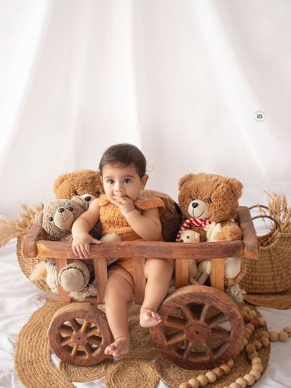 A cute shot of a baby sitting in a rustic wooden cart surrounded by teddy bears, part of our boho setup.