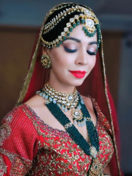 A close-up of a luxurious bridal look. The hair is styled into an elaborate structure that supports a heavy, traditional matha patti, demonstrating how to balance intricate hair artistry with opulent bridal accessories.