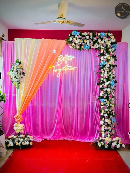This vibrant stage decor uses a playful mix of pink, orange, and yellow drapes. We framed it with a floral L-shaped arch and added a "Better Together" neon sign to create a fun and colorful photo booth area.