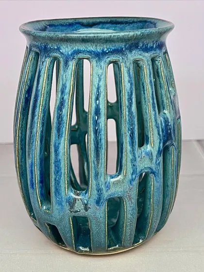 A finished wheel-thrown tea light holder with vertical carved slots. The turquoise glaze pools and breaks over the edges, creating a beautiful effect when lit from within.