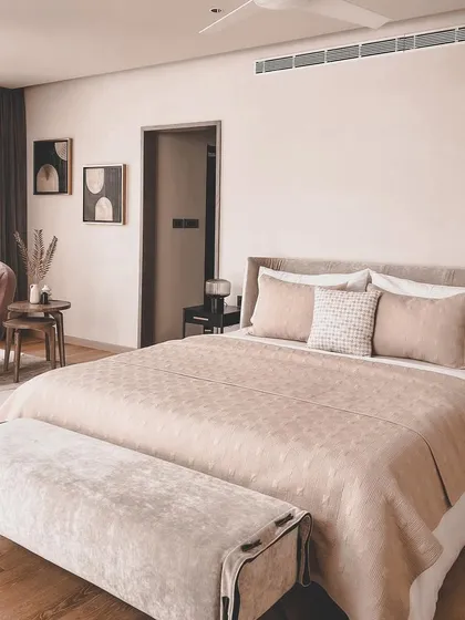 A serene and sophisticated bedroom design featuring a soft, dusty rose and beige color palette. The plush, upholstered bed and bench, combined with the elegant chandelier, create a space that feels both luxurious and restful.