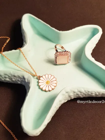 Our starfish trinket tray in a beautiful solid teal color, holding a daisy necklace and a statement ring.