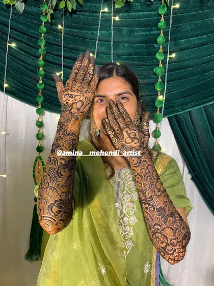A fun and happy shot of a bride showcasing her mehendi, which includes a heart and initial design.